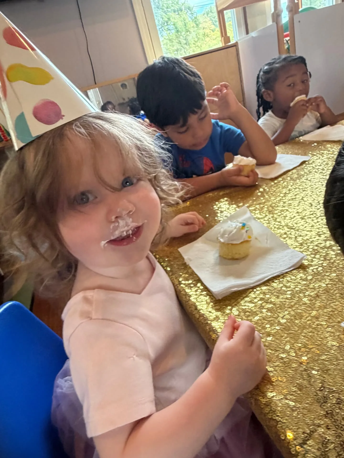 Toddler in a party hat enjoying a birthday cupcake with friends