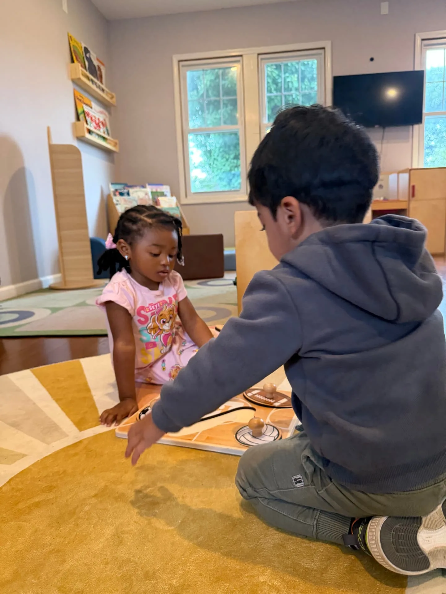 Two children playing with a wooden puzzle on the classroom rug