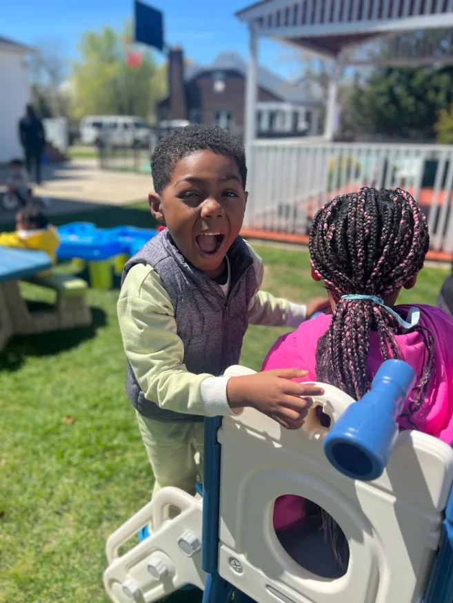 Preschooler laughing with friends on the outdoor play climber